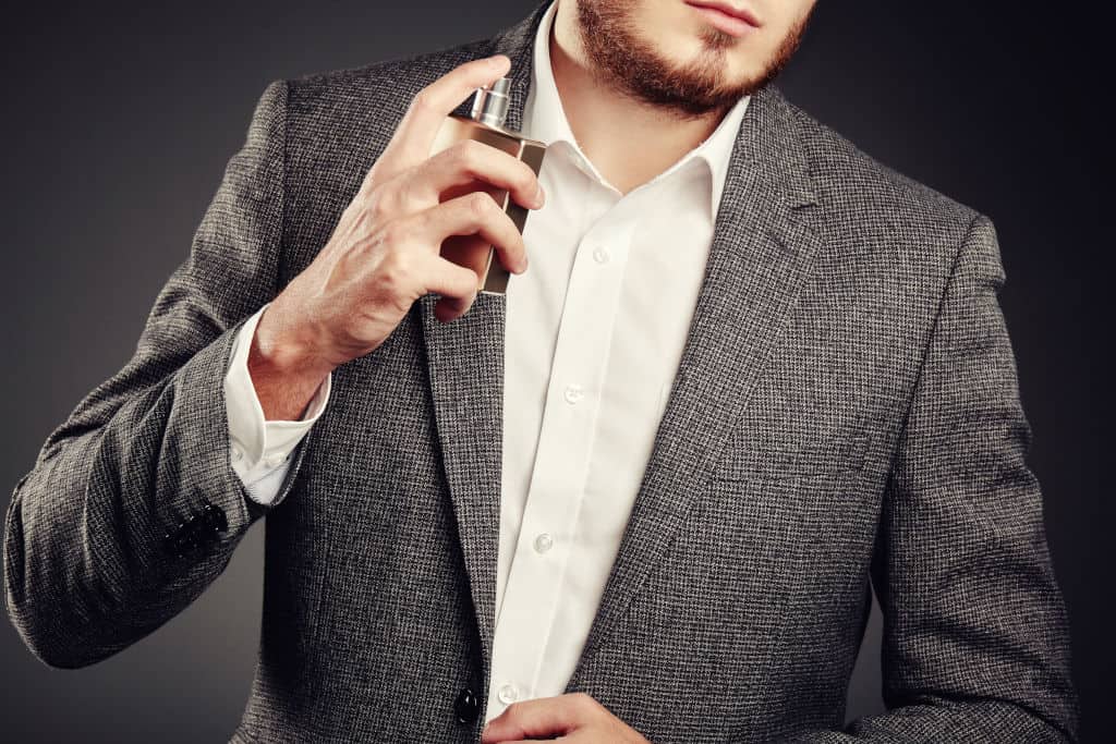 man spraying perfume on his neck and clothes