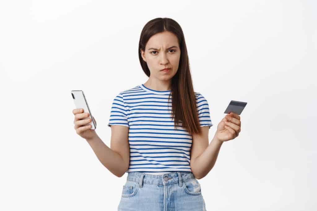 young woman holding a card an a phone looking at camera suspiciously